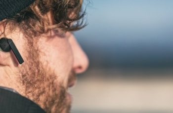 homem na praia utilizando um fone de ouvido bluetooth preto