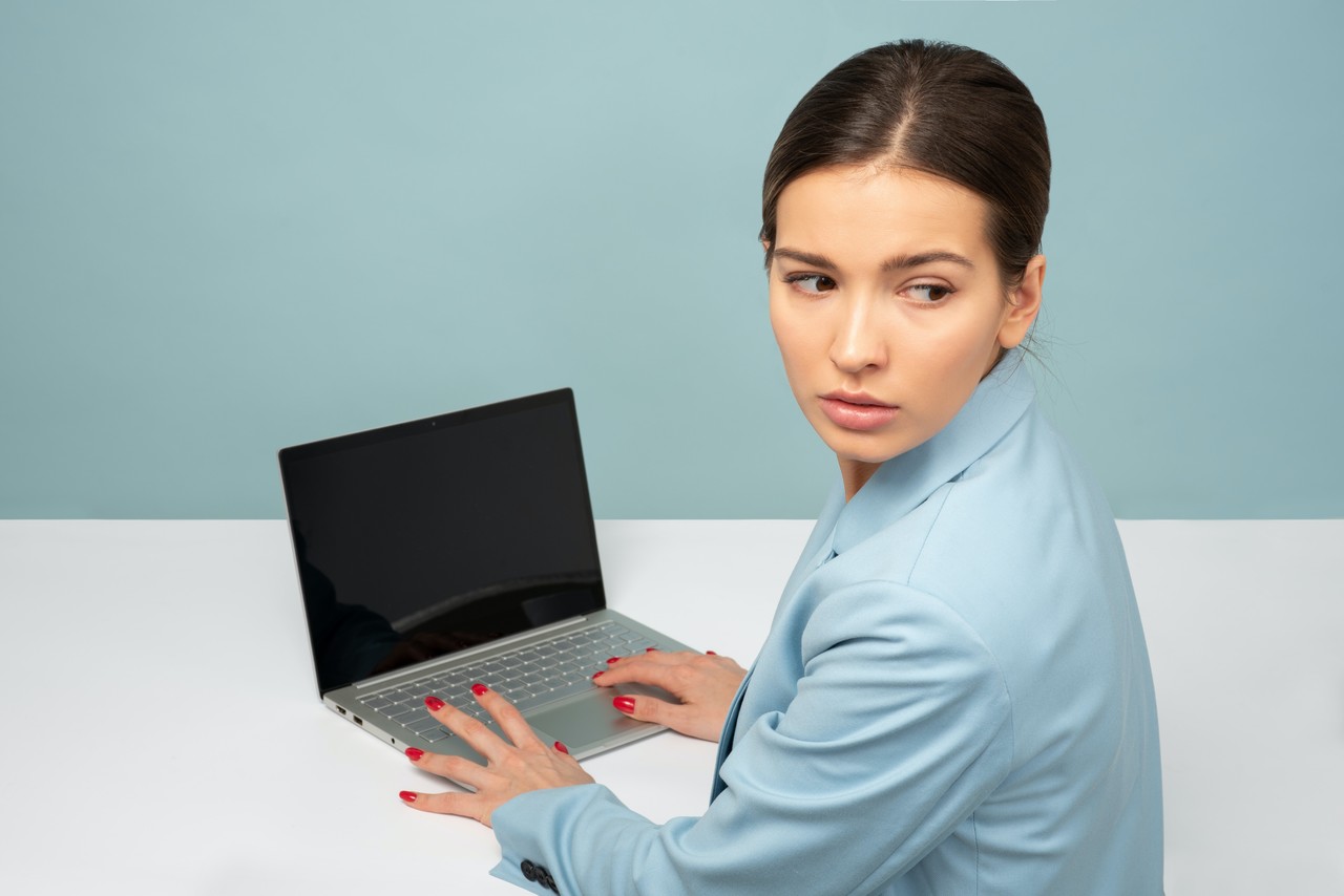 Mulher desconfiada olhando para trás com computador a sua frente sobre uma mesa