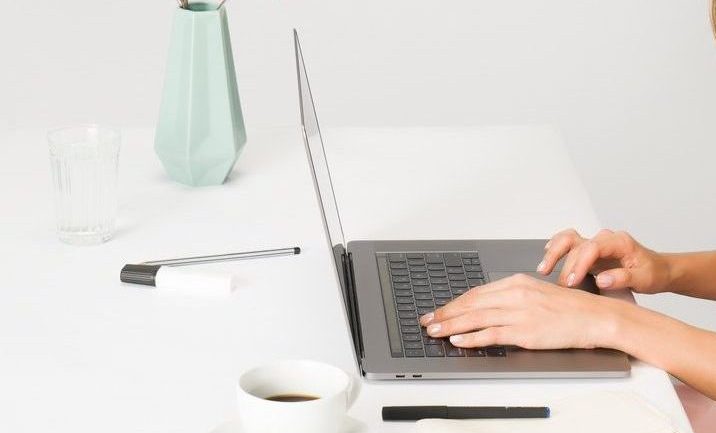 Mulher utilizando scroll do notebook sobre uma mesa branca