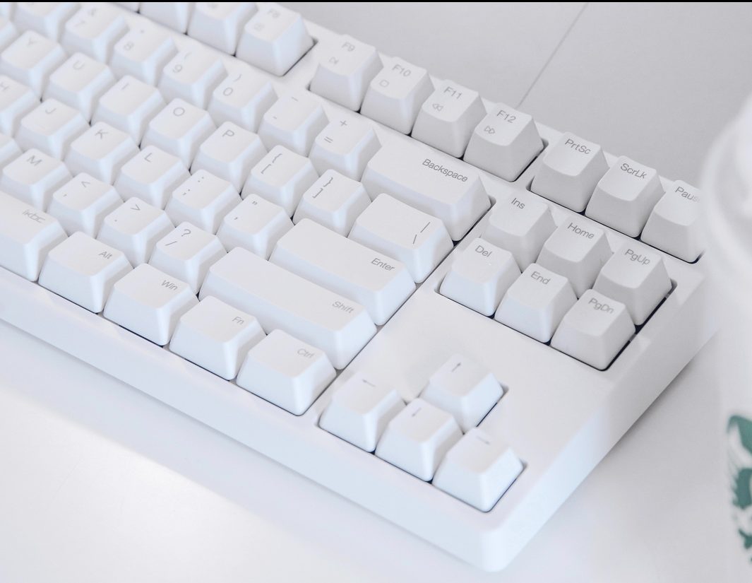Teclado branco com teclas como Scroll lock ao lado de um copo de café