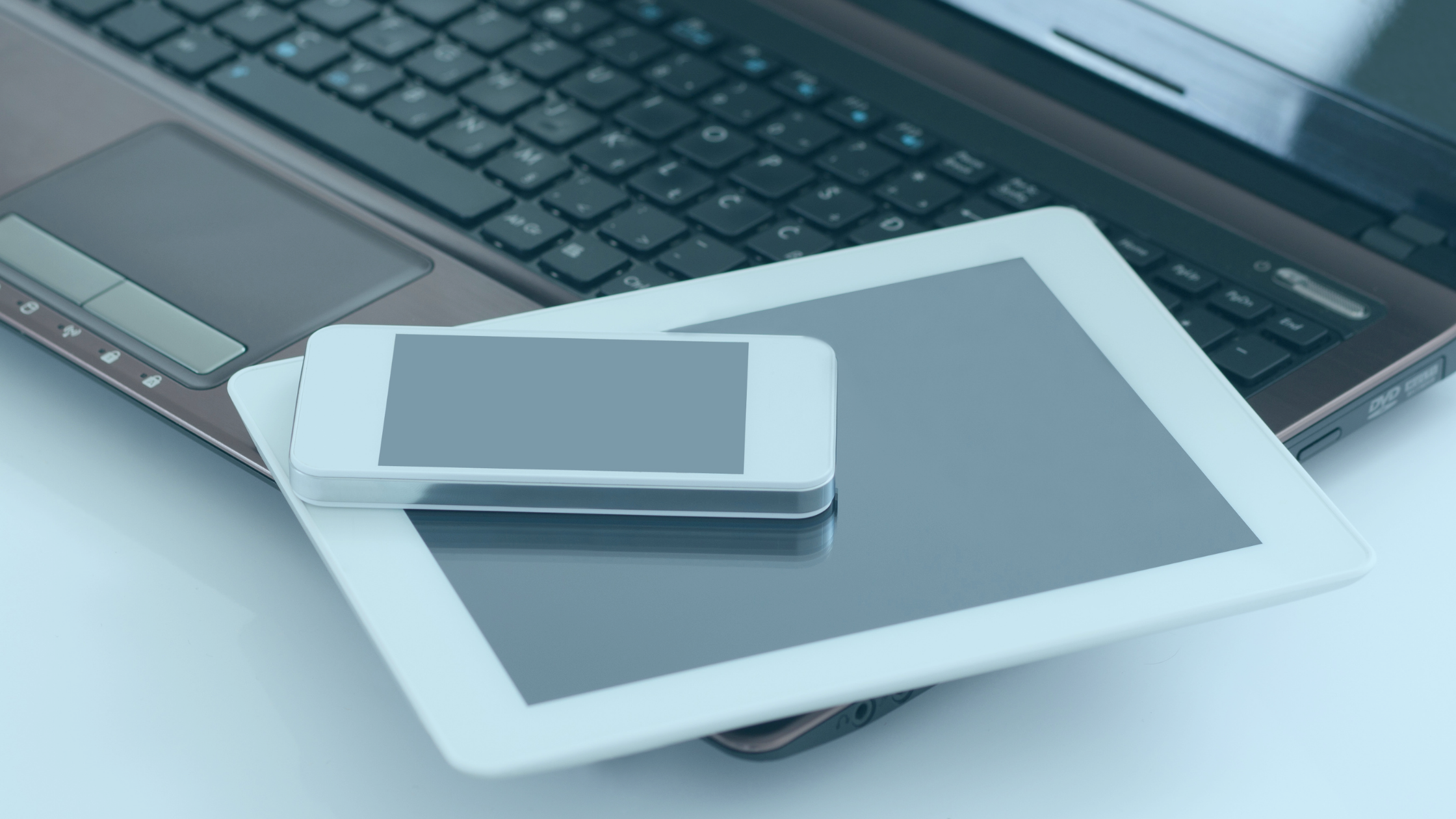 Close de um teclado de notebook. Sobre ele repousam um tablet e um smartphone.