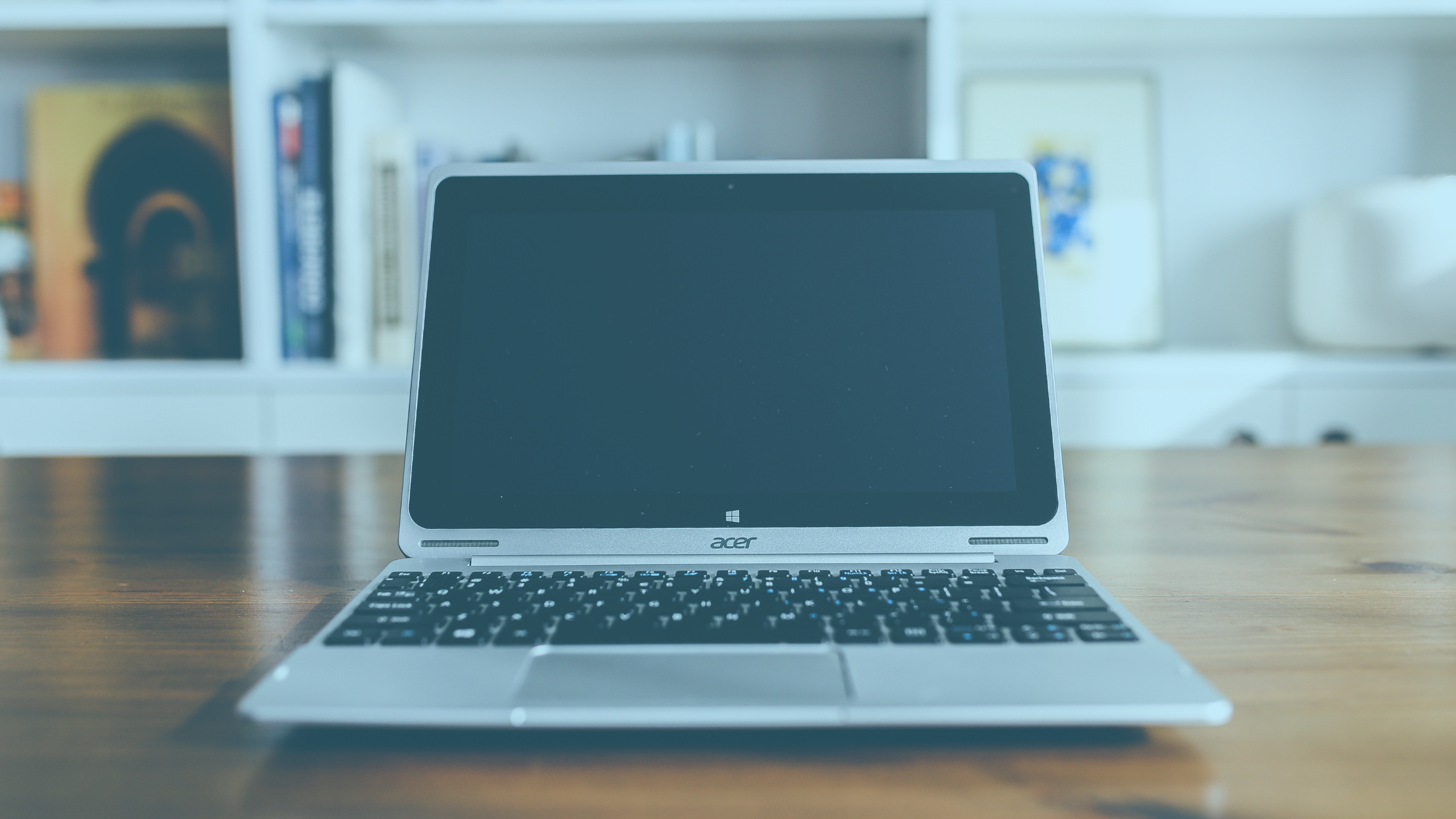 Imagem de um notebook aberto sobre uma mesa, a tela encontra-se desligada.